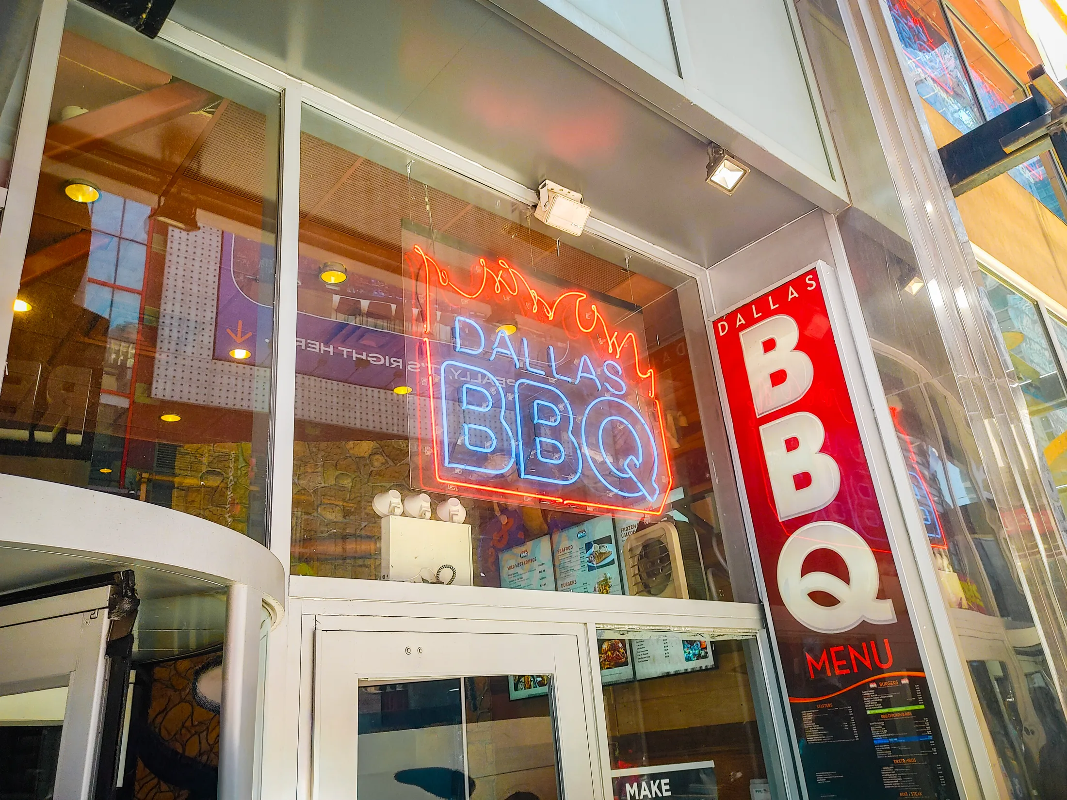 Red and blue Dallas BBQ neon glowing inside a glass storefront