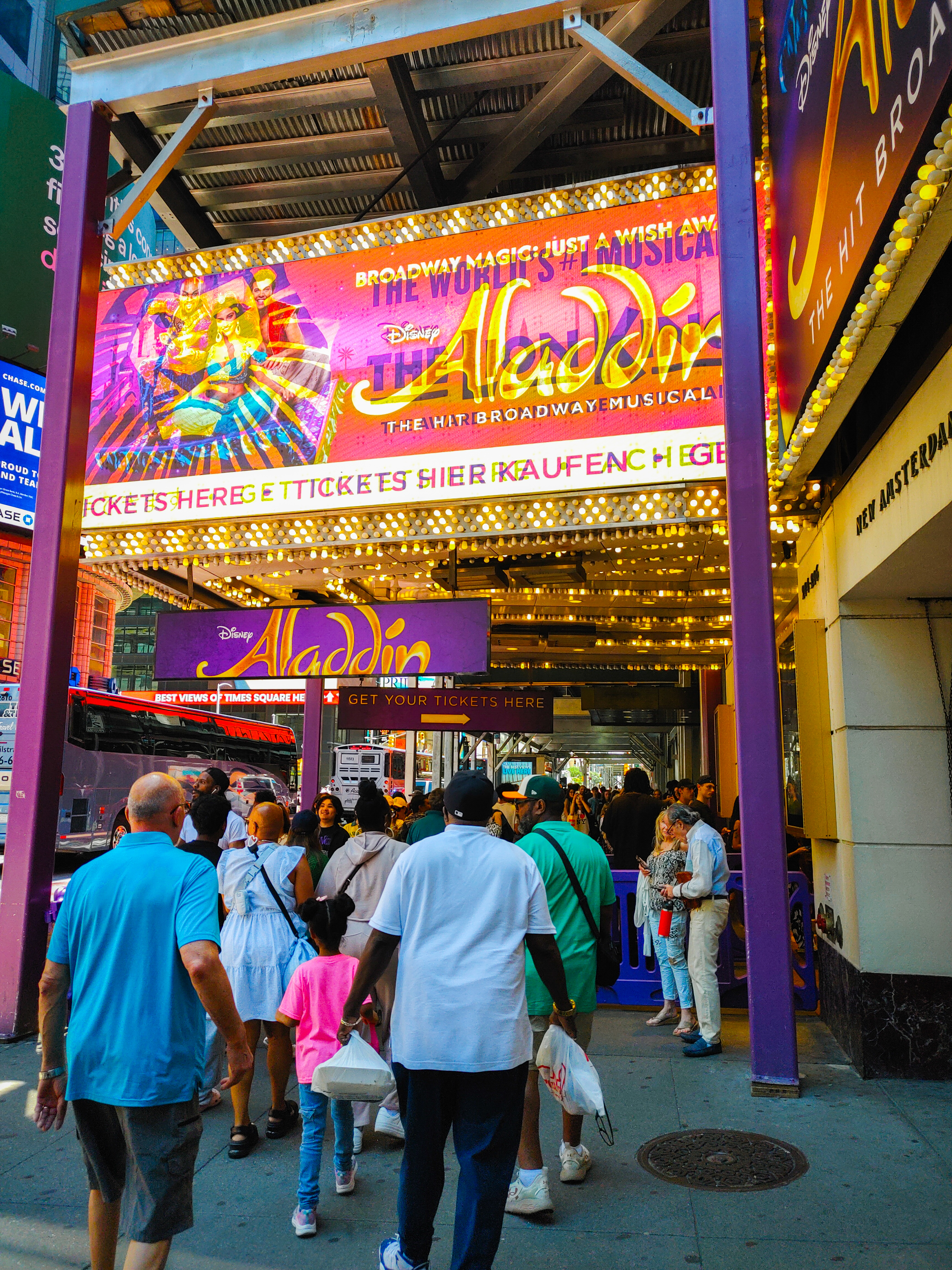 Crowd moving beneath the vivid purple and gold marquee for Aladdin on Broadway