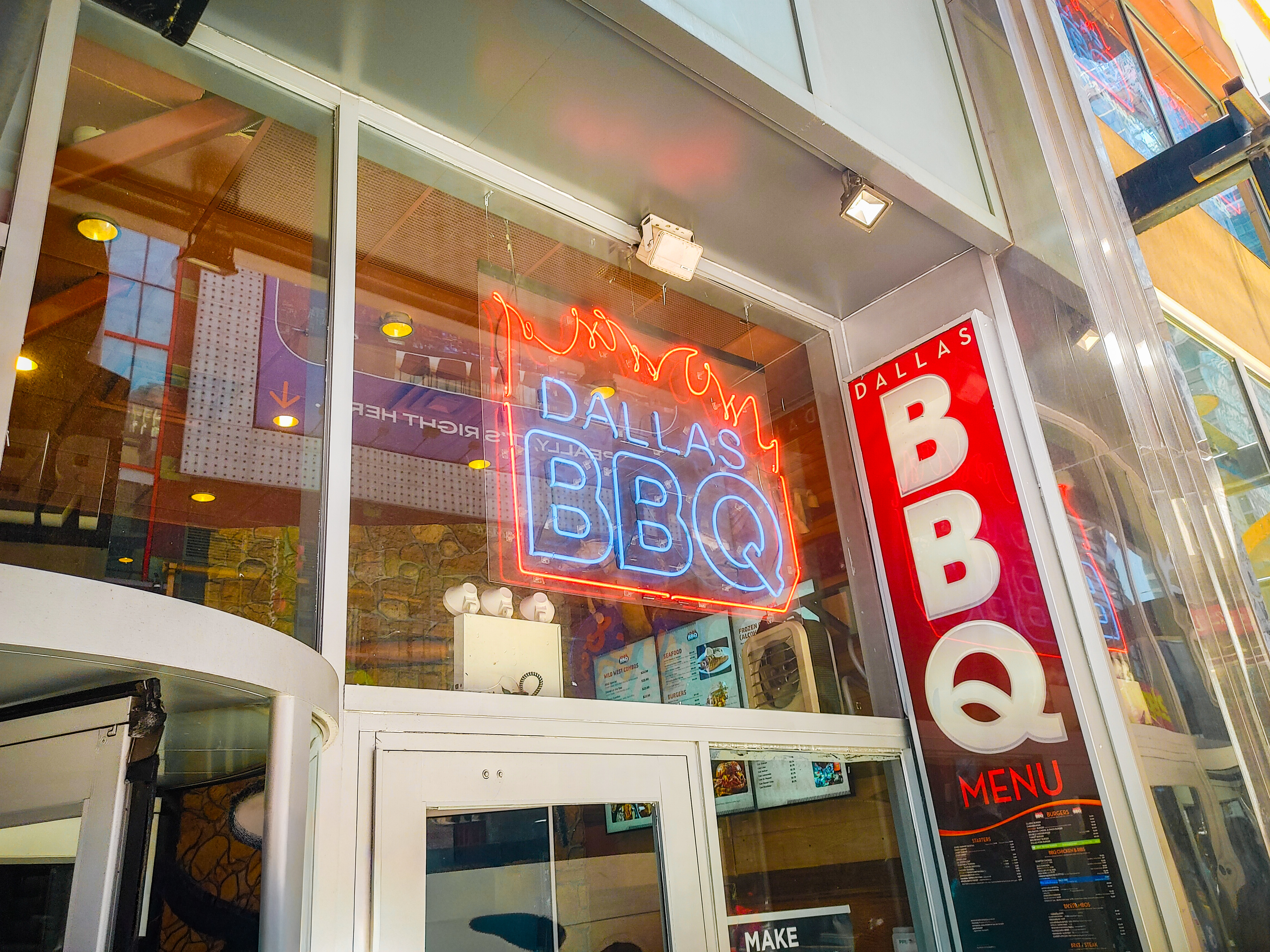 Red and blue Dallas BBQ neon glowing inside a glass storefront